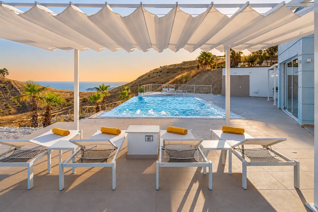 Die Liegen unter der Pergola, der Pool und das Meer